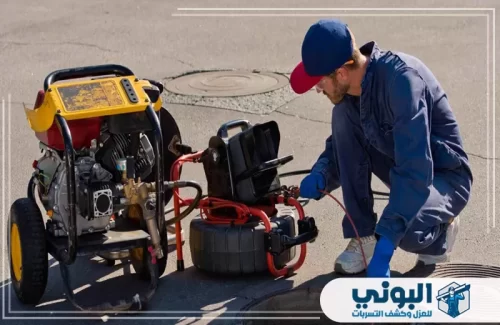 تسليك مواسير مجاري في الرياض 0500805875 البوني عامل صيانة يستخدم جهاز تحكم وخرطوم شفط عمودي لتطهير فتحة صرف صحي محاطة بشريط تحذيري.