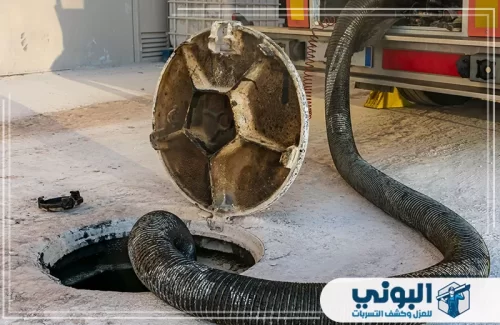 تنظيف المجاري في الرياض 0500805875 البوني خرطوم شفط ضخم متصل بشاحنة صيانة يسحب الرواسب من داخل فتحة صرف صحي دائرية مفتوحة.