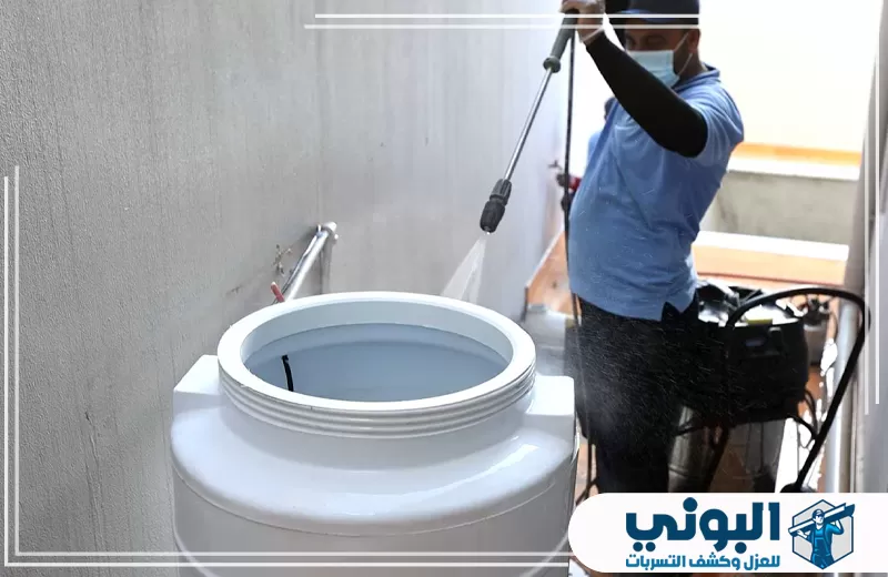 عامل يوجه غسالة ضغط إلى خزان بلاستيكي علوي أثناء تنظيف الخزانات العلوية بالقصيم