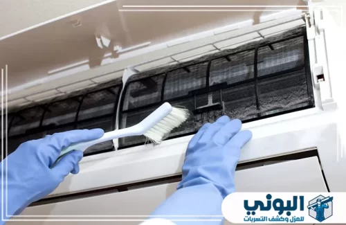 تنظيف مكيفات فلبينيين بالدمام 0500805875 شركة البوني عامل يرتدي قفازات زرقاء ويستخدم فرشاة بيضاء لتنظيف فلتر مكيف الهواء الداخلي المتسخ، صيانة ضرورية.